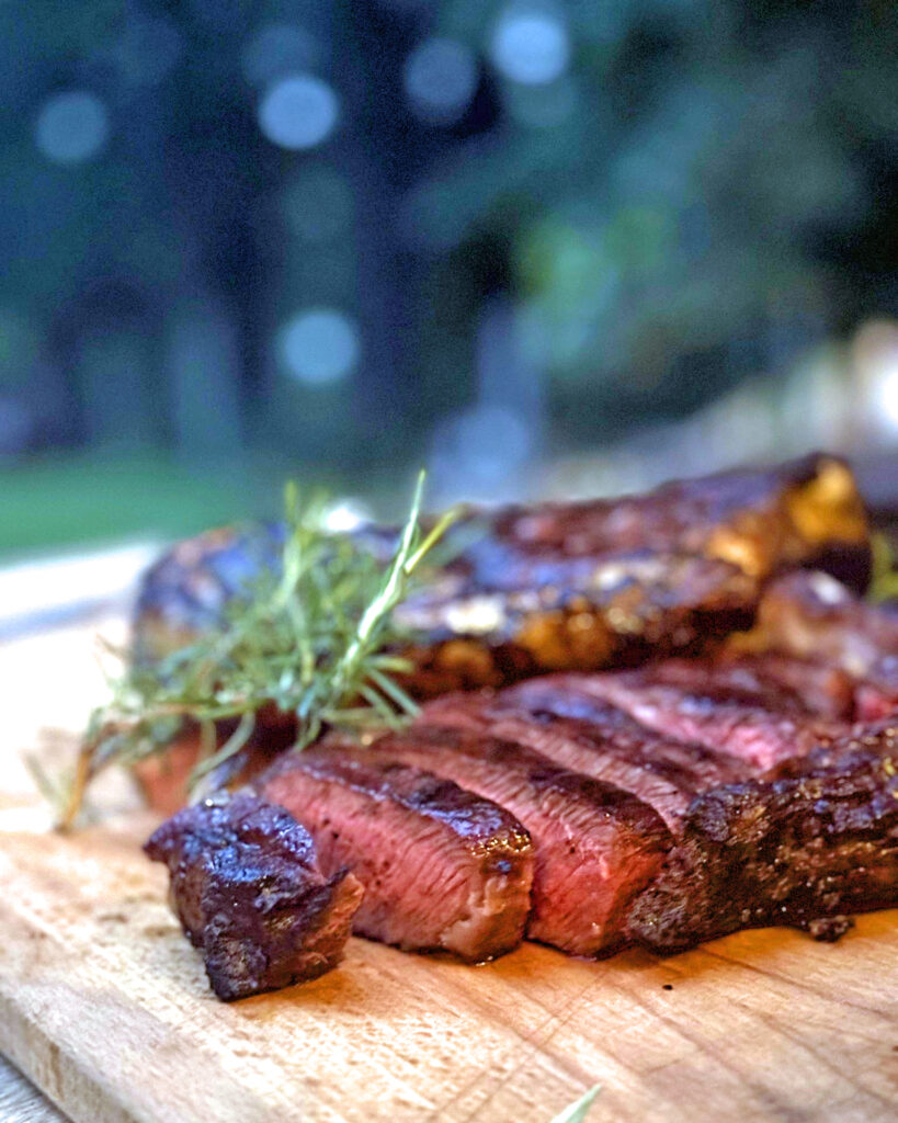 Gegrilltes Entrecôte vom Dexter-Rind, medium-rare auf Holzbrett serviert mit frischen Kräutern